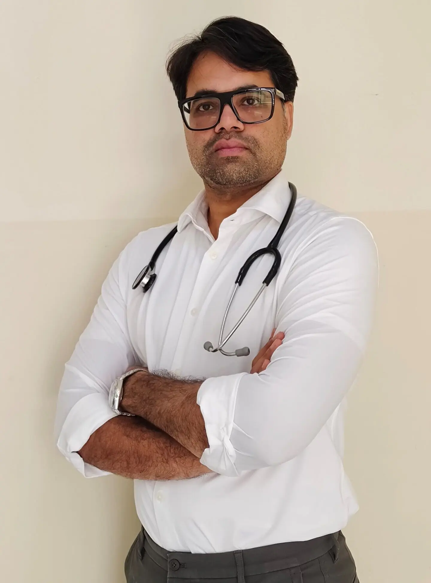 Doctor wearing stethoscope and glasses, confidently posing with folded arms indoors.