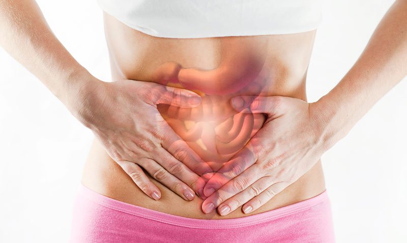 Person holding stomach in pain with a digital overlay of the human digestive system showing inflammation.